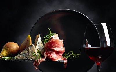 Glass of red wine with traditional mediterranean snacks. Prosciutto or spanish jamon with blue cheese, pears and rosemary.